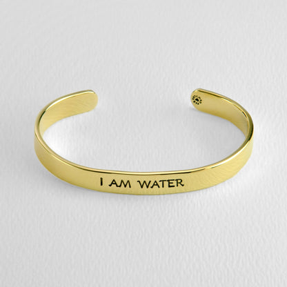 Brass bracelet with 'I AM WATER' engraving on a light gray background