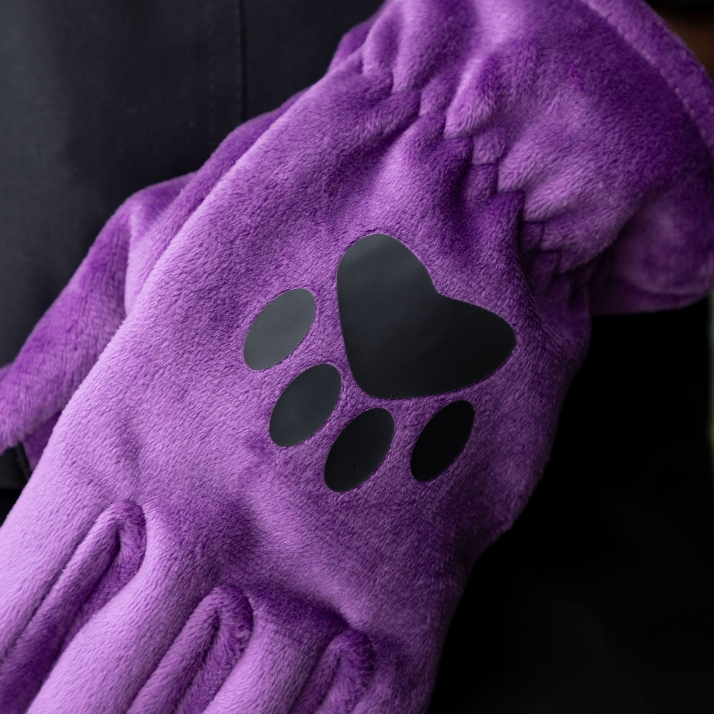 Purple fleece glove with black paw print design on a dark background.
