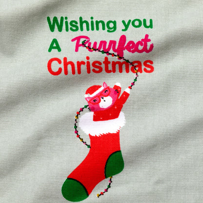 Printed design of a cat in a red stocking with text 'Wishing you a purrfect Christmas' on a fabric background.

