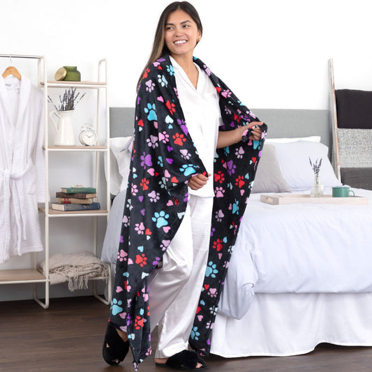 A woman standing in a bedroom setting with a colorful paw print and heart fleece blanket wrapped around her shoulders.