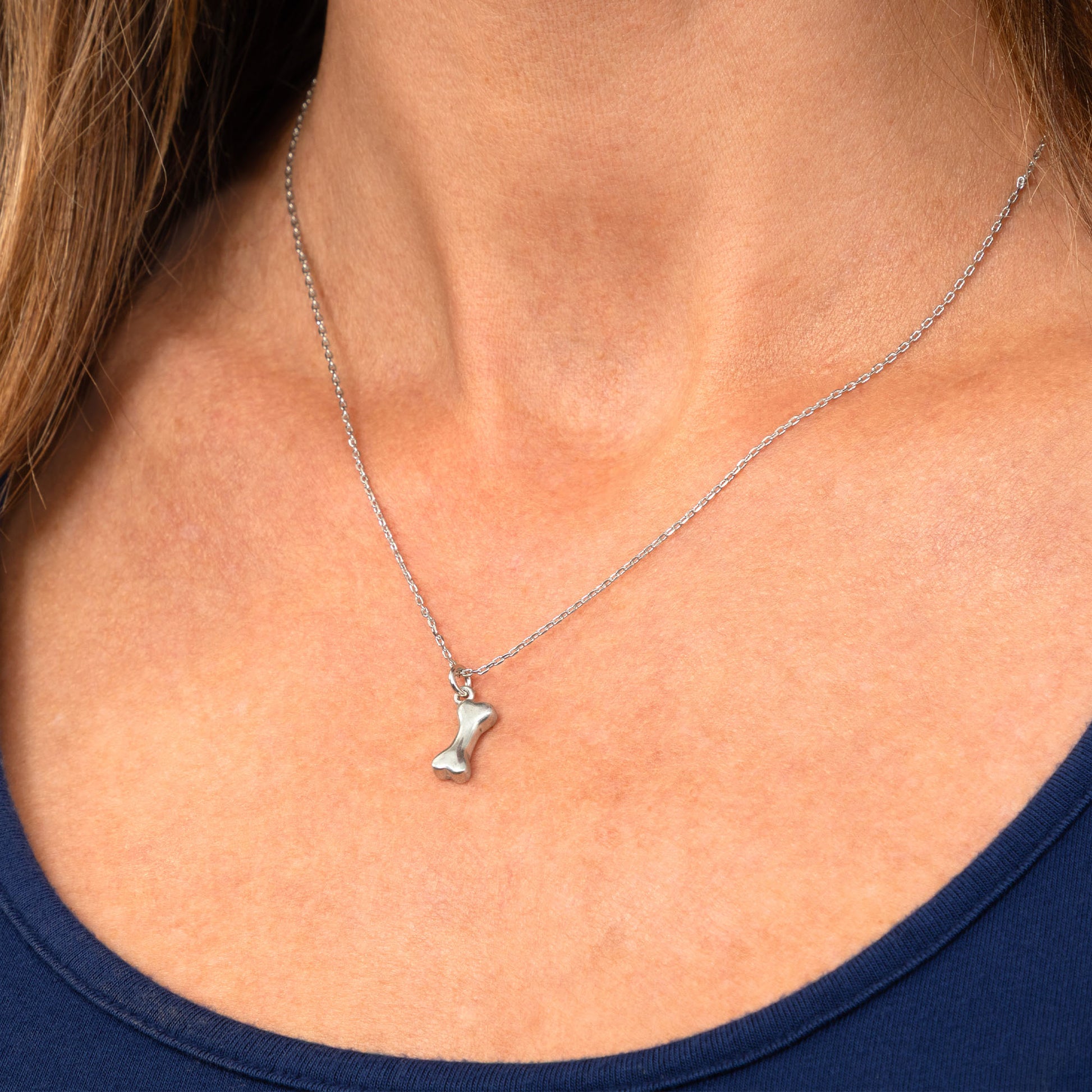 A close-up of a person's neck and chest wearing a delicate silver chain necklace with a small silver pendant, paired with a navy blue top.