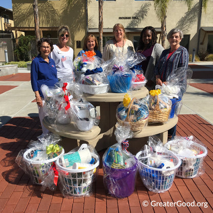 Group of people standing around a table with gift baskets on a sidewalk.