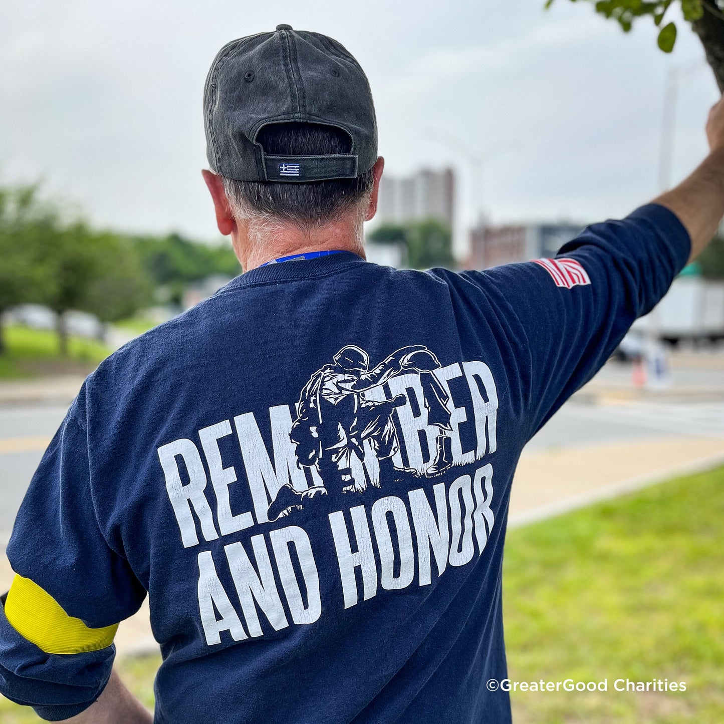 Person wearing a navy blue shirt with 'Remember and Honor' text and a logo, outdoors.