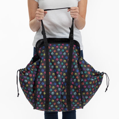 A person holding a large black drawstring collapsible bag with a colorful repeating paw print pattern, shown against a plain white background.