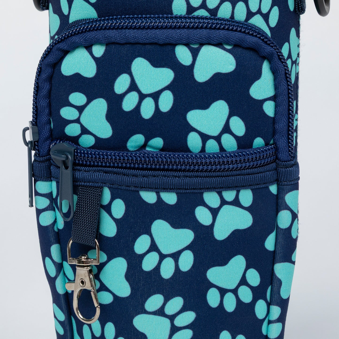 Close-up of a navy blue bag with a repeating light blue paw print pattern, featuring two zippered pockets and a silver metal clip.