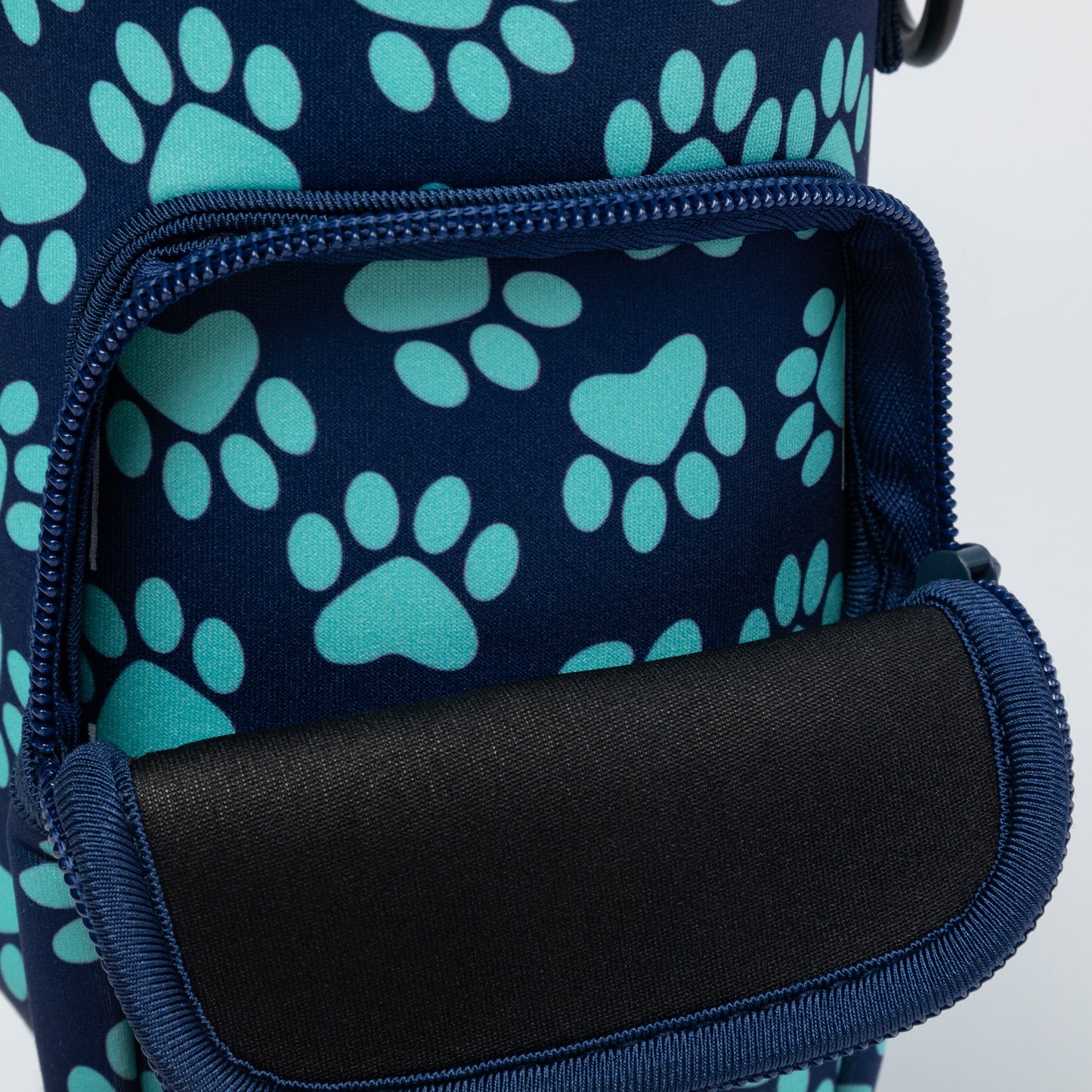Close-up of a navy blue bag with a repeating teal paw print pattern and an open front zip pocket showing a black interior lining.