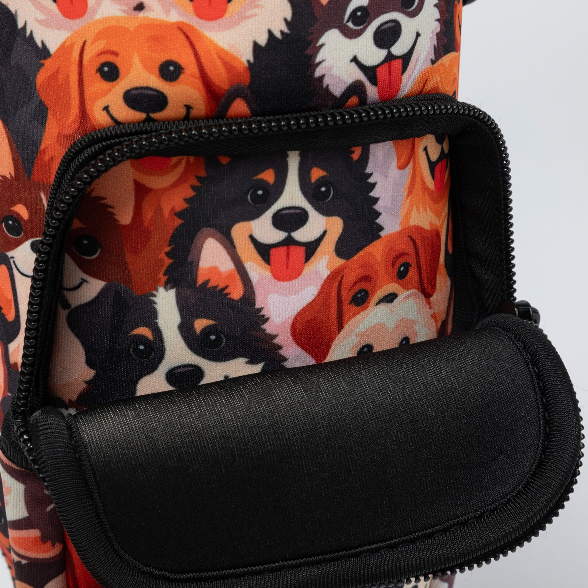 Close-up of a backpack or bag with a black front zip pocket and a printed fabric body featuring cartoon dog faces in orange, black, white, and brown on a light background.