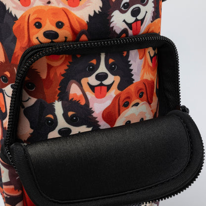 Close-up of a backpack or bag with a black front zip pocket and a printed fabric body featuring cartoon dog faces in orange, black, white, and brown on a light background.