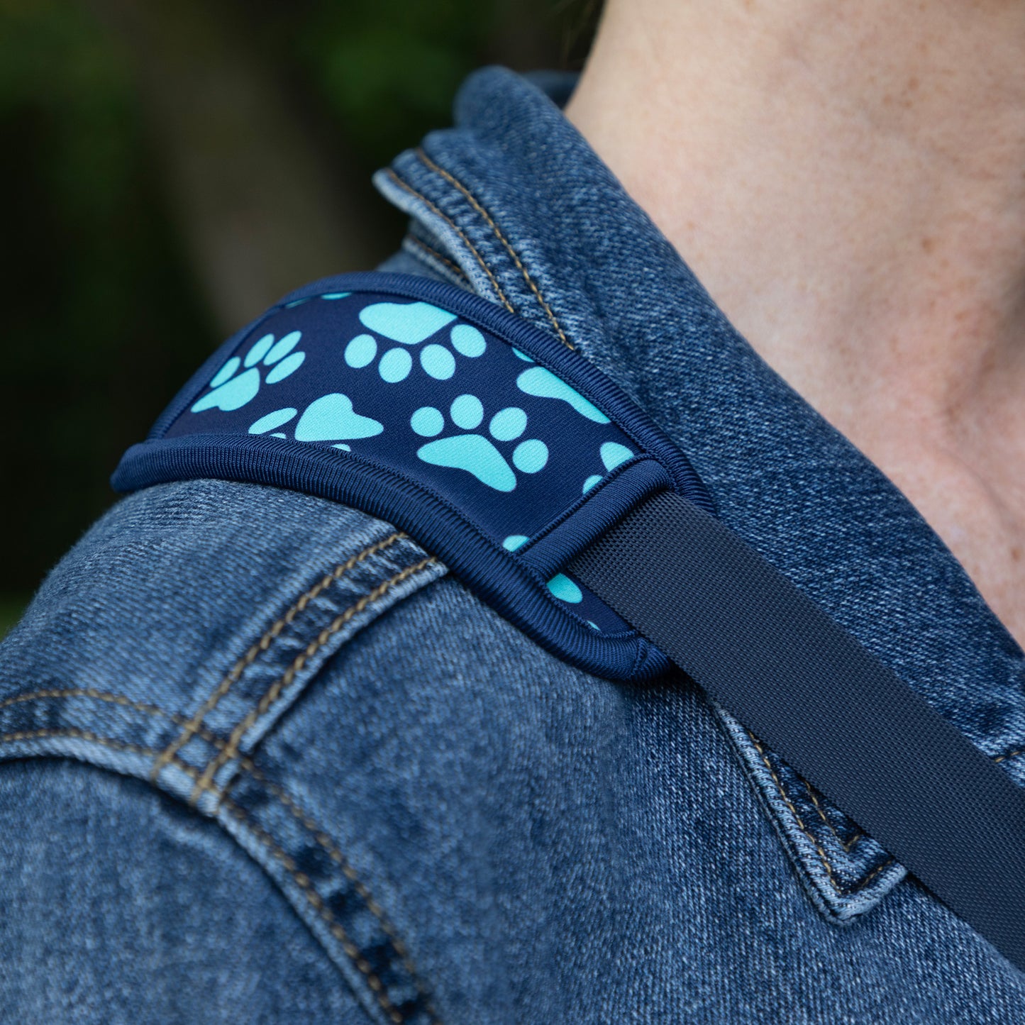 Close-up of a harness strap worn over a person's shoulder, featuring a navy blue fabric with a light blue paw print pattern and a dark gray webbing strap.