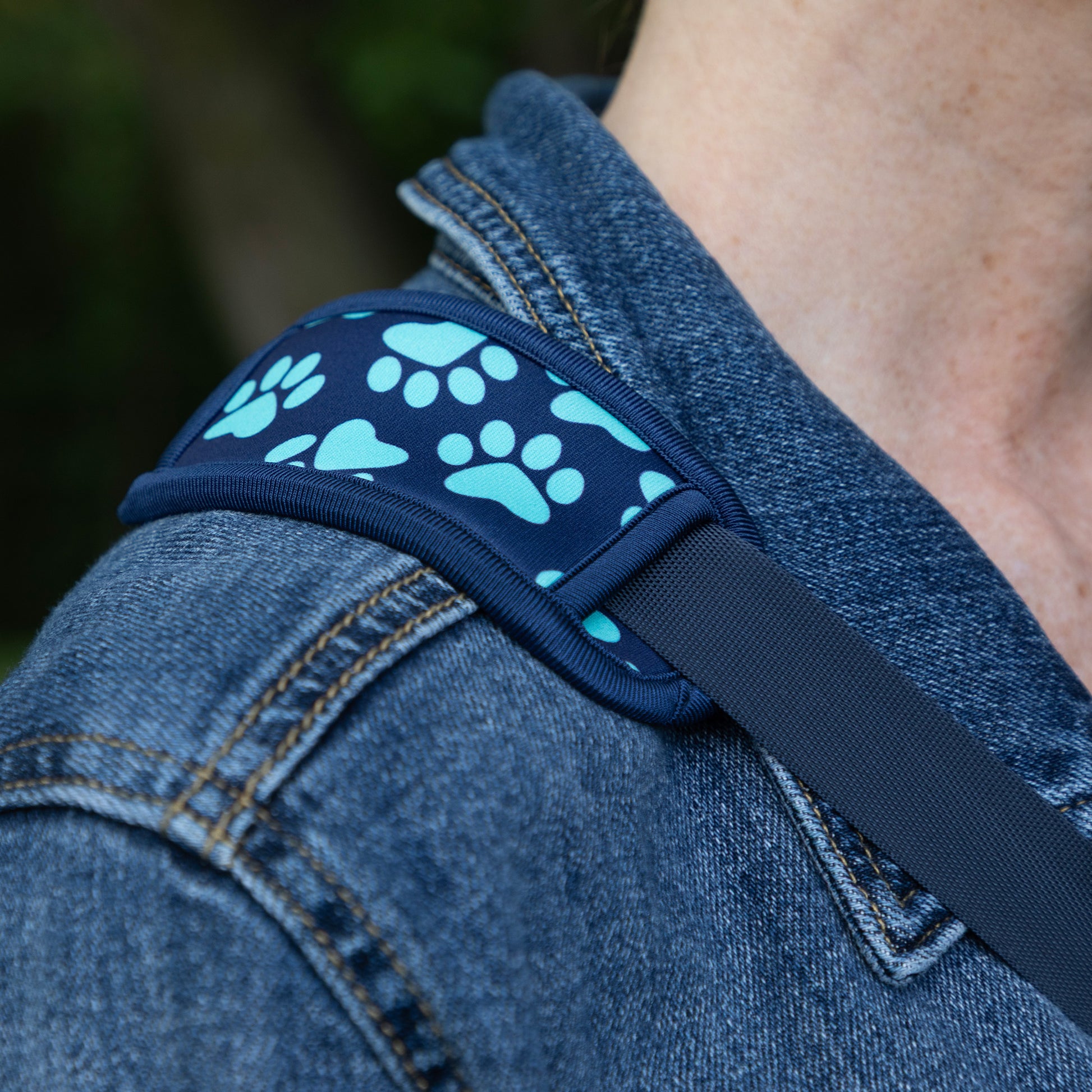 Close-up of a harness strap worn over a person's shoulder, featuring a navy blue fabric with a light blue paw print pattern and a dark gray webbing strap.
