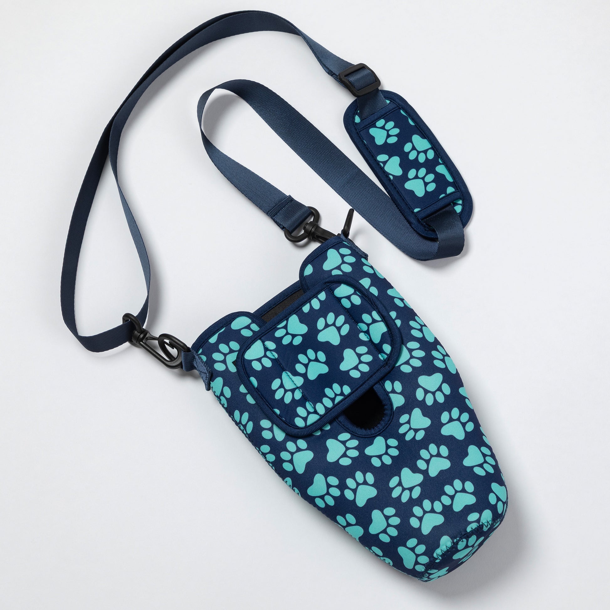 A navy blue pet carrier bag with a repeating mint green paw print pattern, featuring a matching adjustable shoulder strap and padded hip pad, shown on a clean white background.