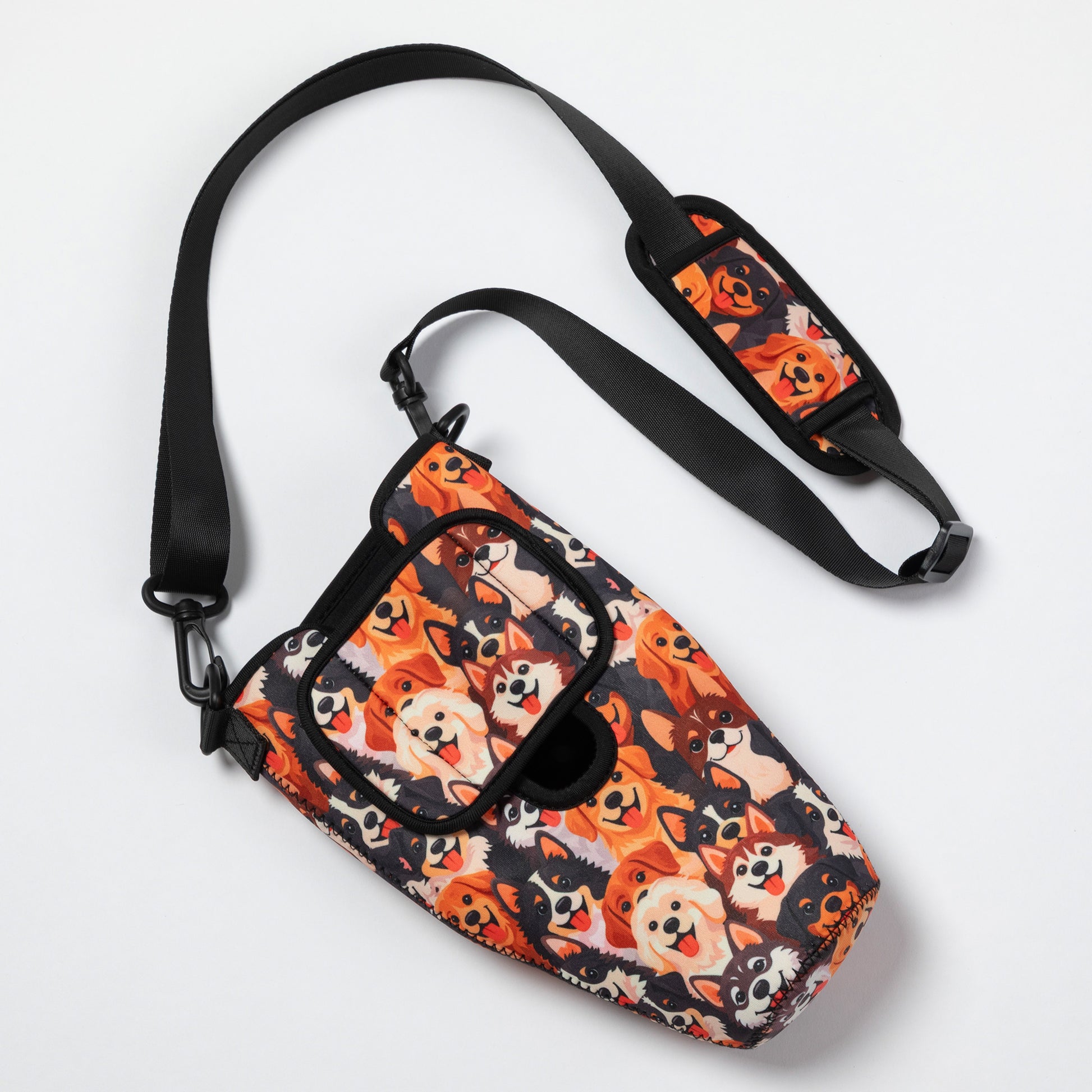 A small crossbody bag with a black adjustable strap, featuring a dense cartoon dog print in orange, black, cream, and white on a clean white background.