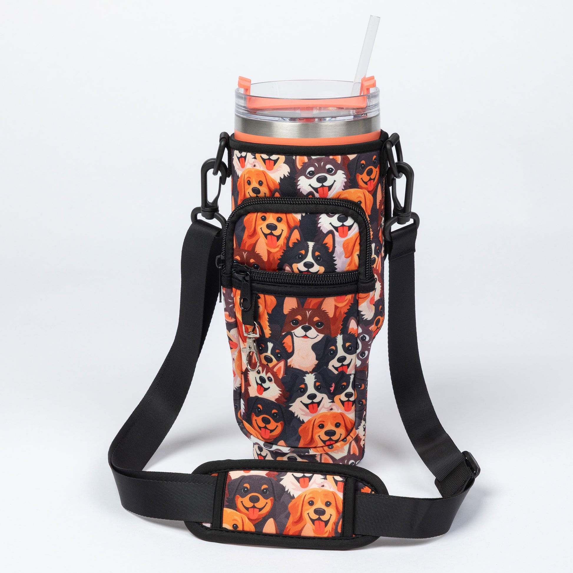 A black insulated tumbler sleeve with an all-over dog print, shown with a clear-lidded tumbler and straw. The sleeve includes a front zip pocket and an adjustable shoulder strap, photographed on a clean white studio background.