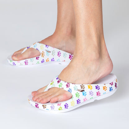 White sandals with colorful paw prints worn by a person on a light gray background