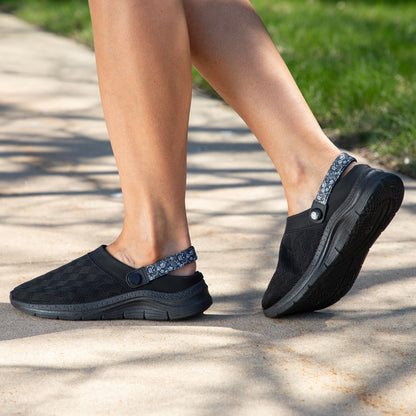 Black slip-on shoes worn outdoors on a concrete surface with grass in the background