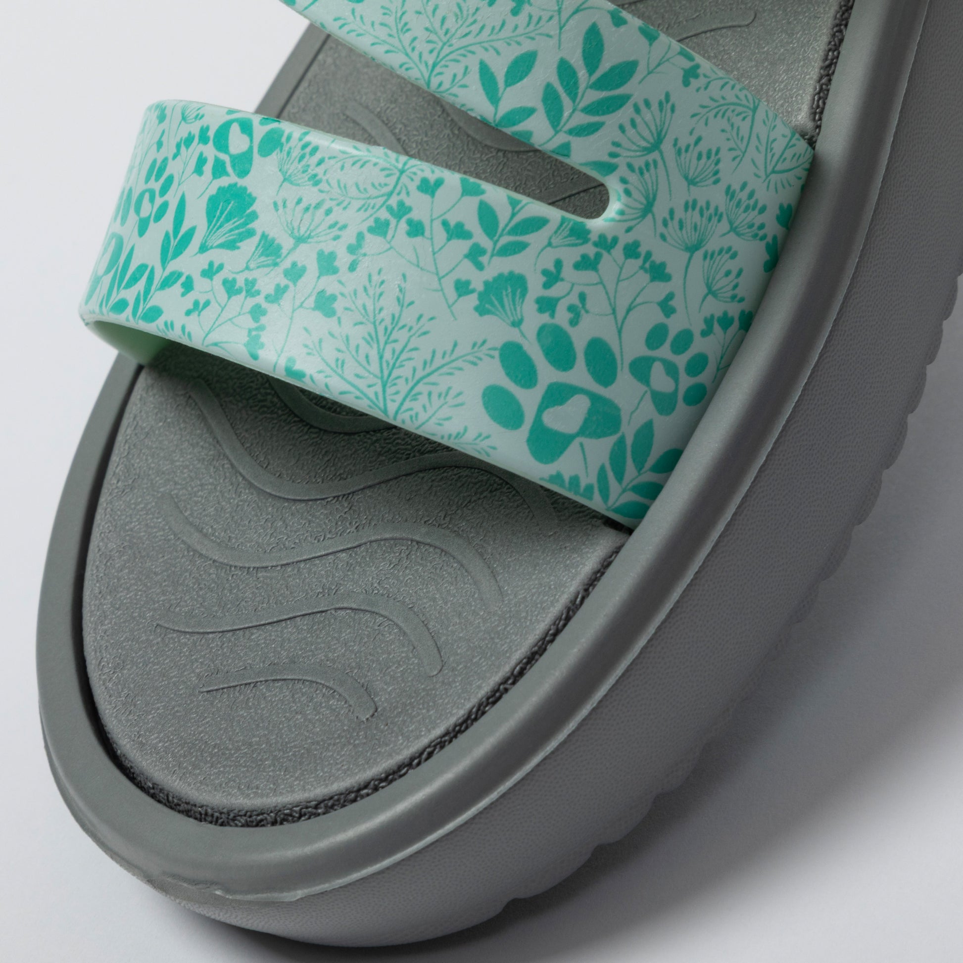 Gray sandal with a green floral strap on a light gray background