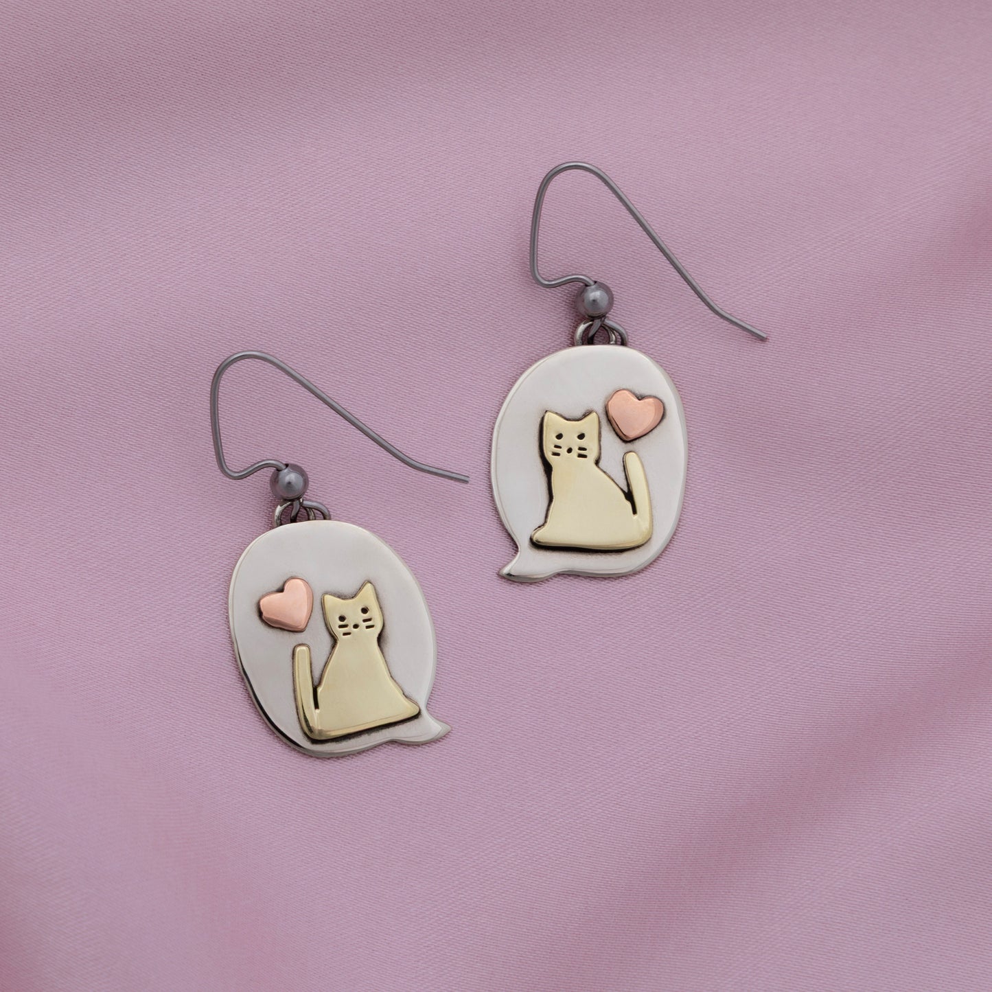 Cat-themed earrings with heart designs on a pink background