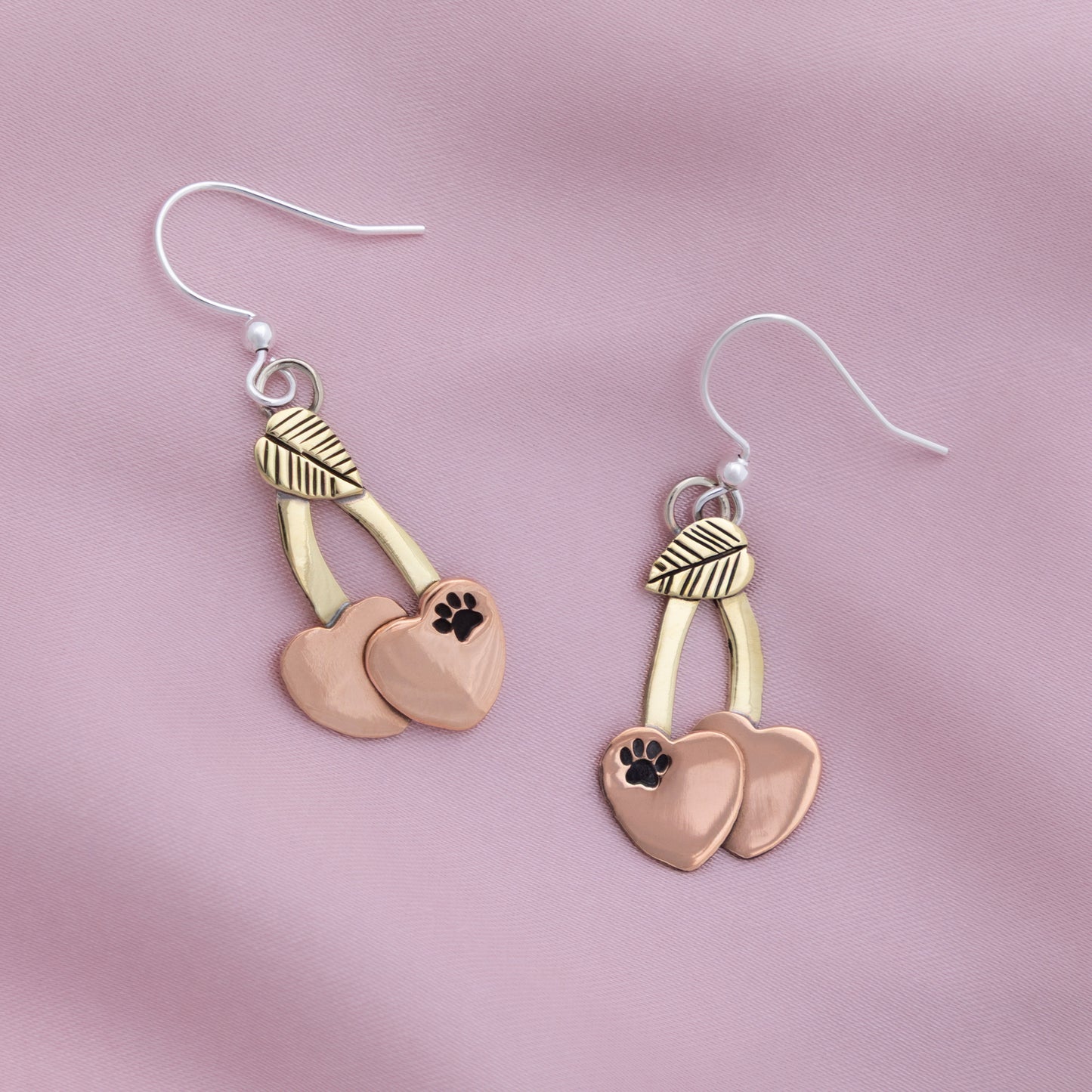 Pair of earrings with heart and paw print design on a pink background