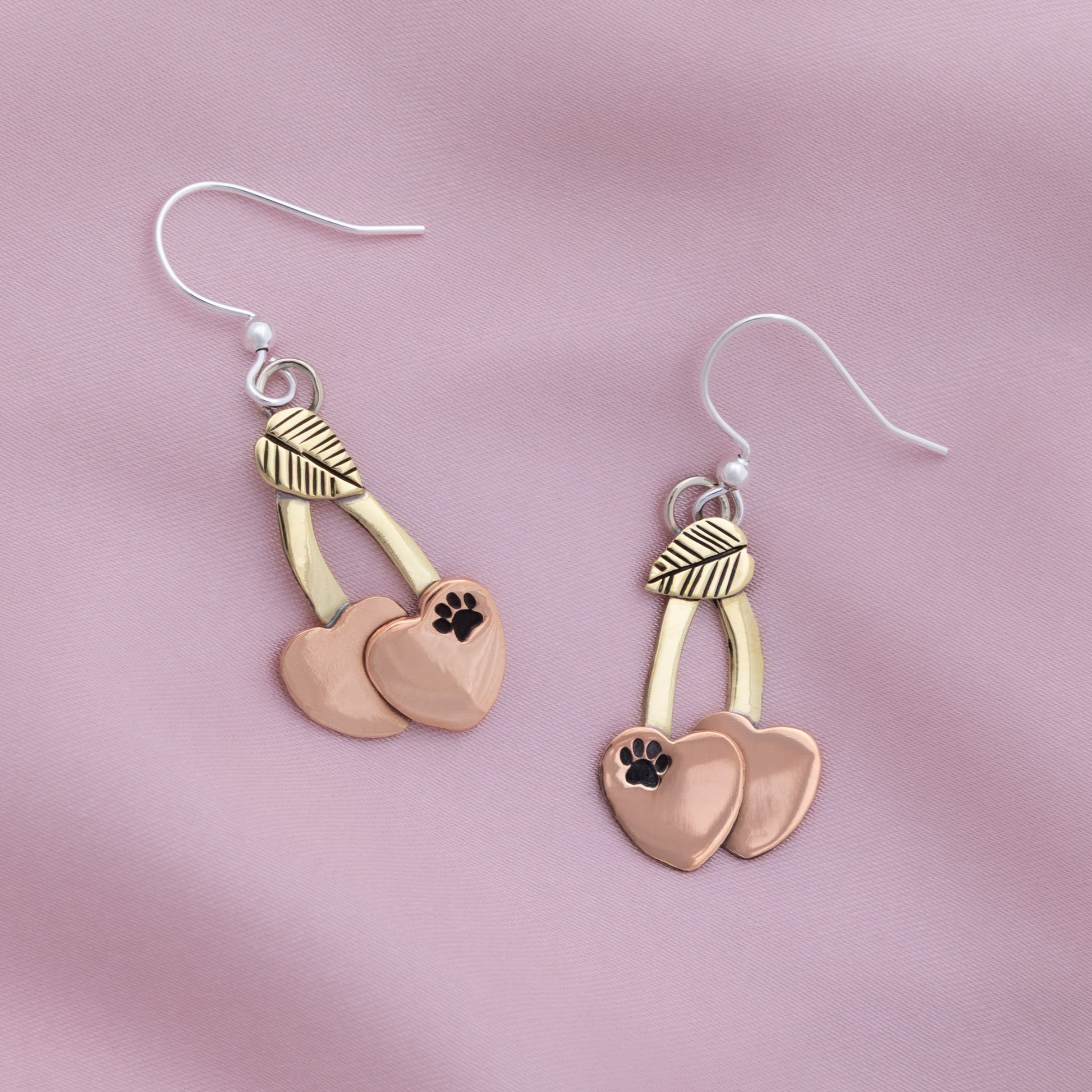 Pair of earrings with heart and paw print design on a pink background