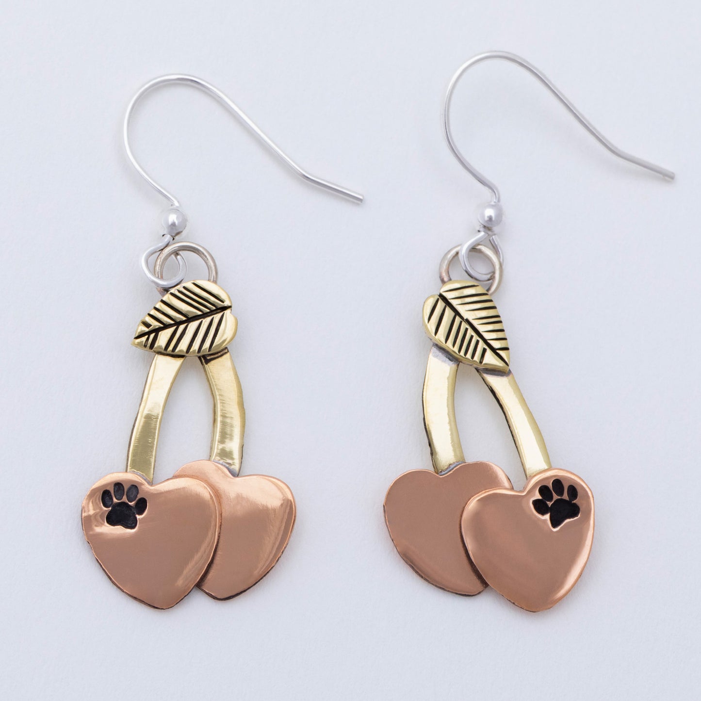 Cherry shaped mixed metal earrings with a small paw print, on a white background.