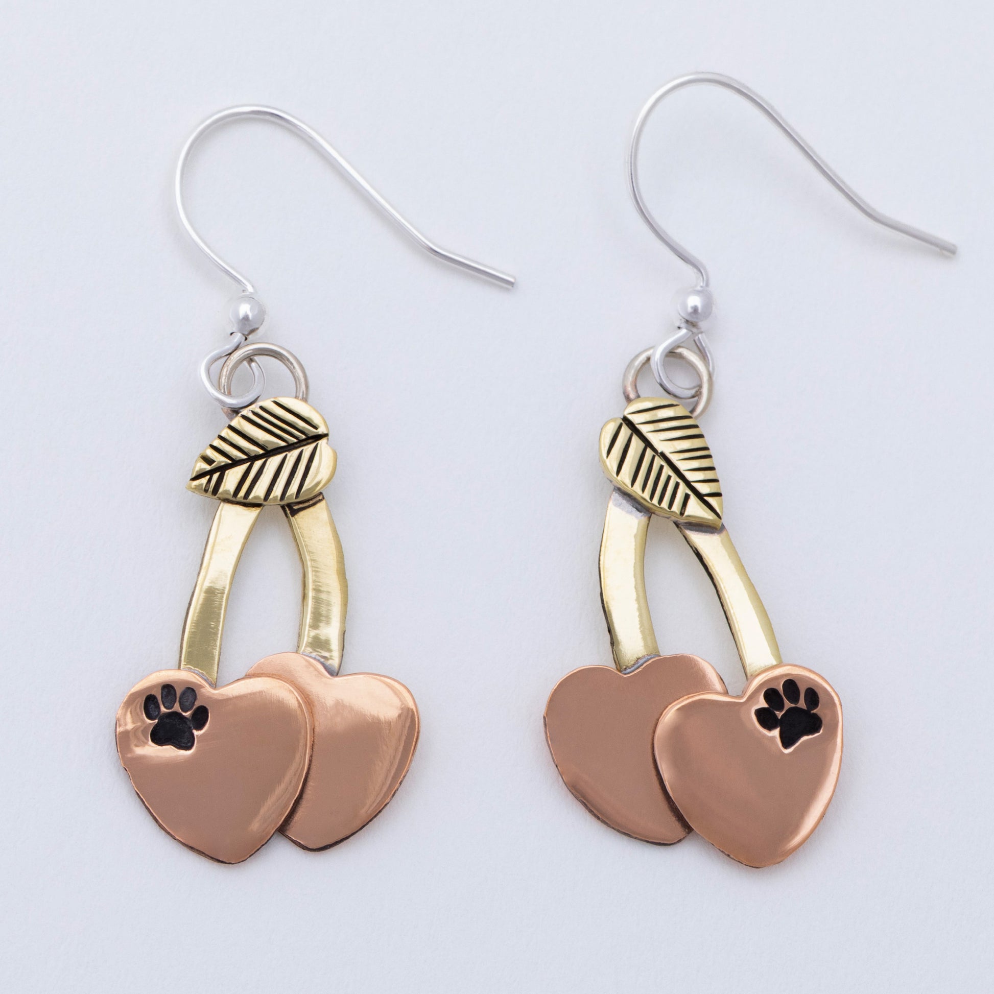 Cherry shaped mixed metal earrings with a small paw print, on a white background.