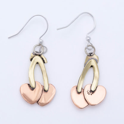 Pair of earrings with brass and copper heart-shaped/ cherry shaped pendants on a light background.