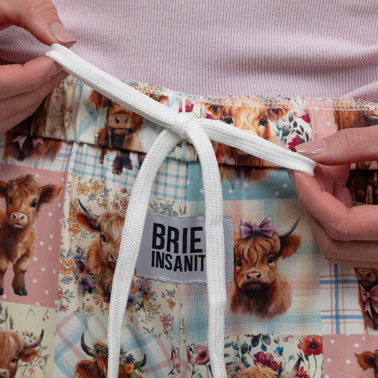 Quilted lounge pants with cow illustrations and a visible brand label, held by hands.