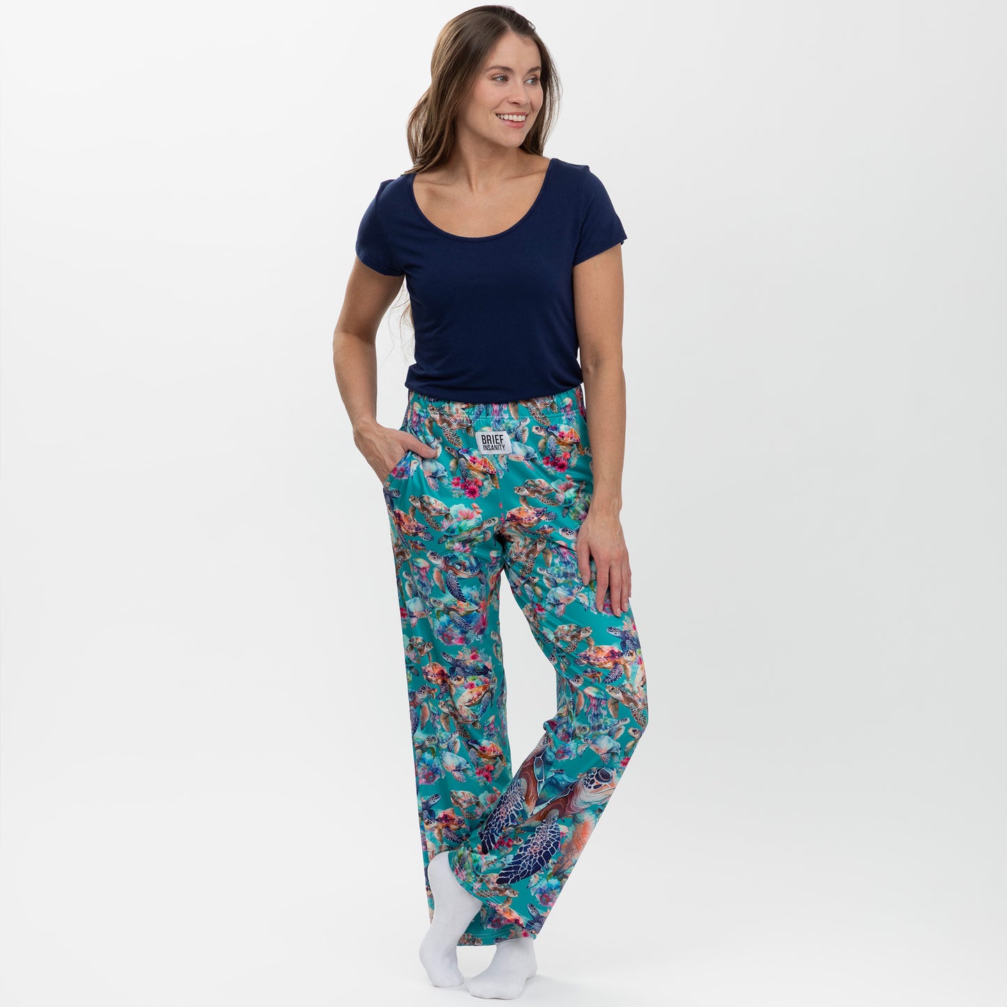 Woman wearing a navy blue top and colorful floral and sea turtle print pants on a white background