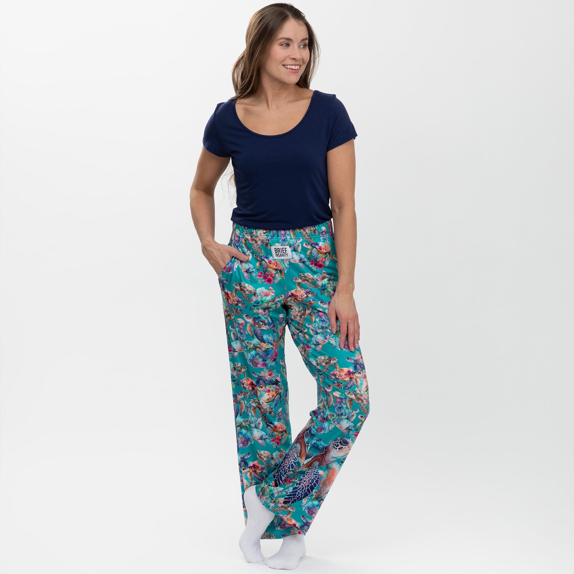 Woman wearing a navy blue top and colorful floral and sea turtle print pants on a white background