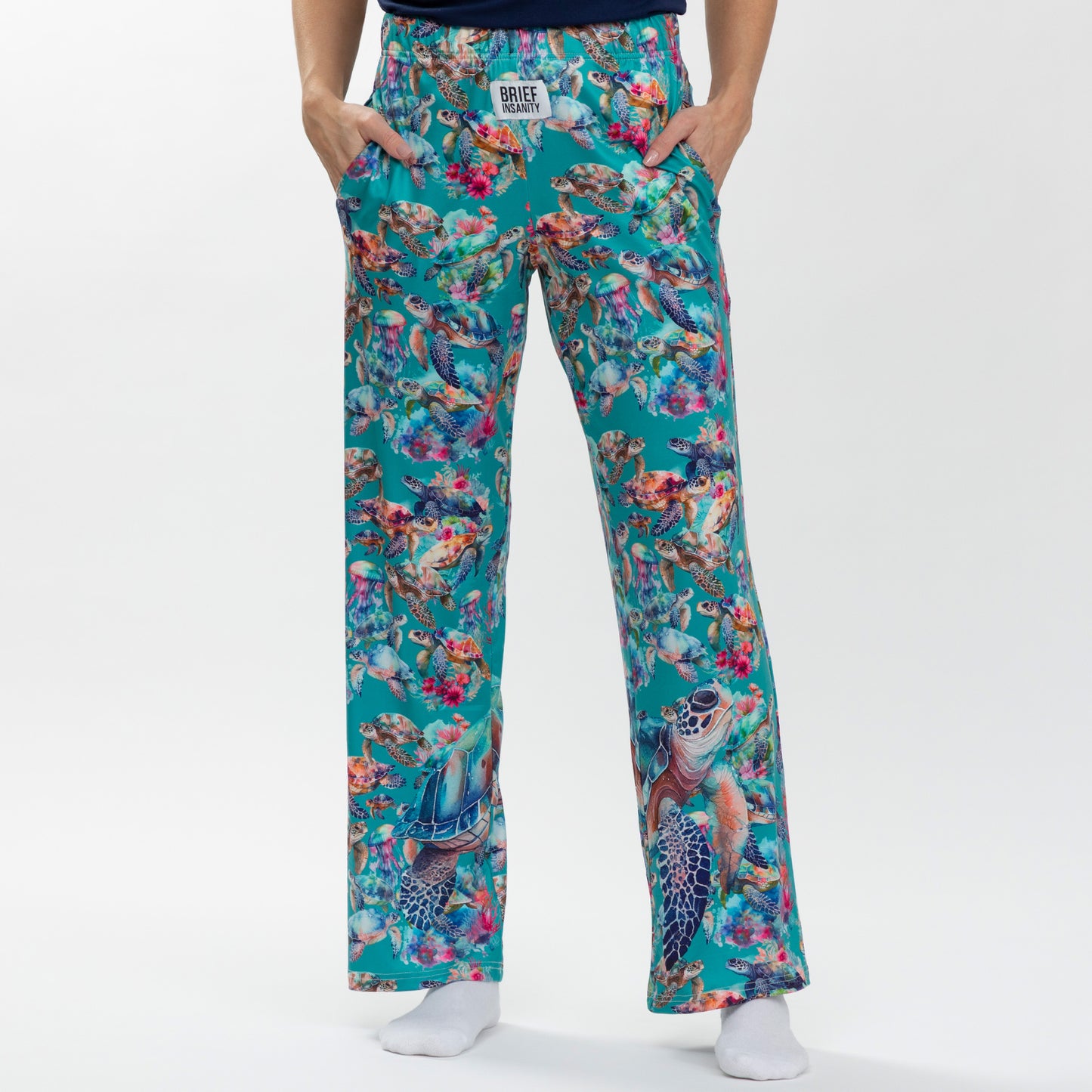 Colorful floral-patterned pants with sea turtles worn by a person on a white background