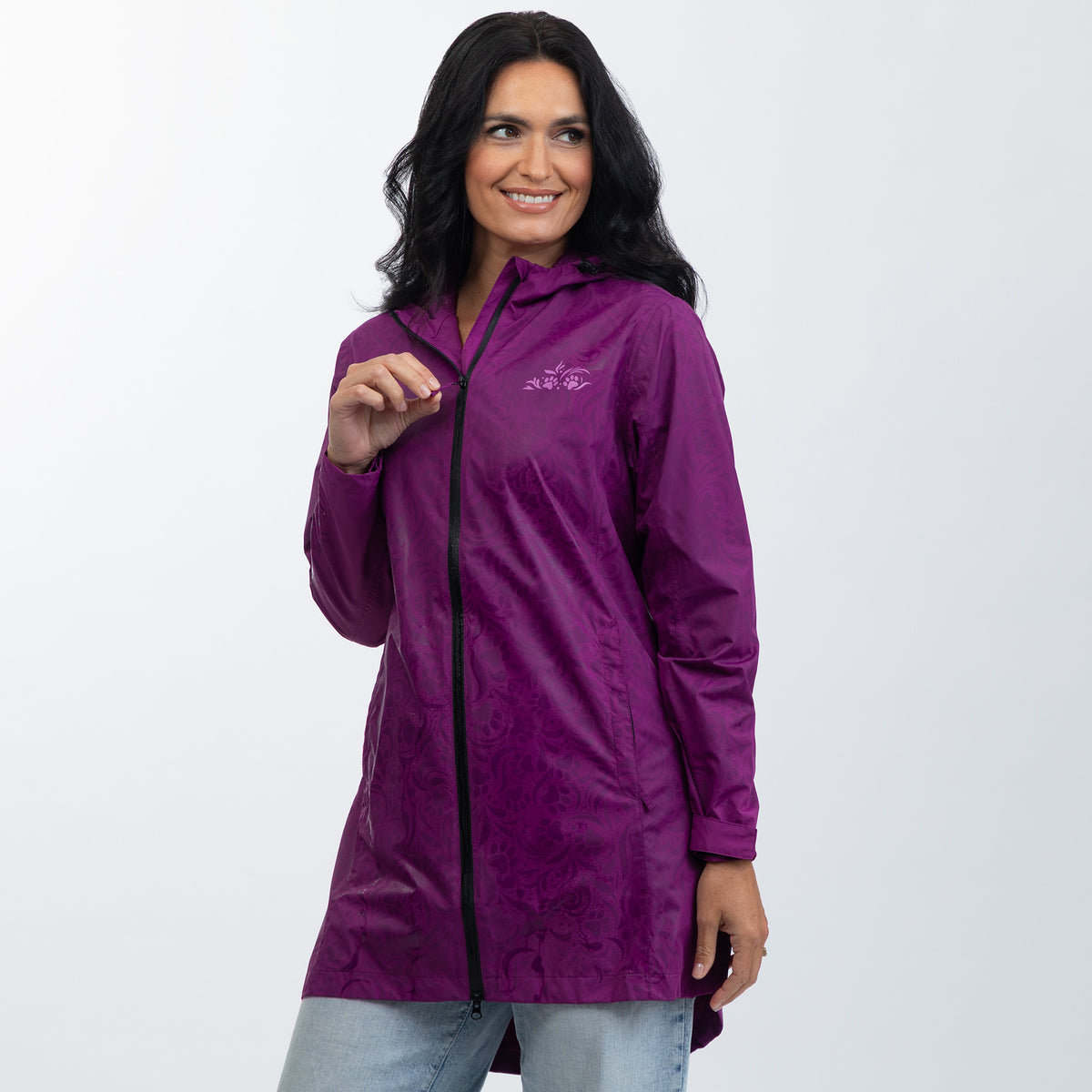 A woman wearing a purple lightweight hooded jacket with a black front zipper and a subtle tonal damask pattern, paired with light blue jeans, against a plain white studio background.