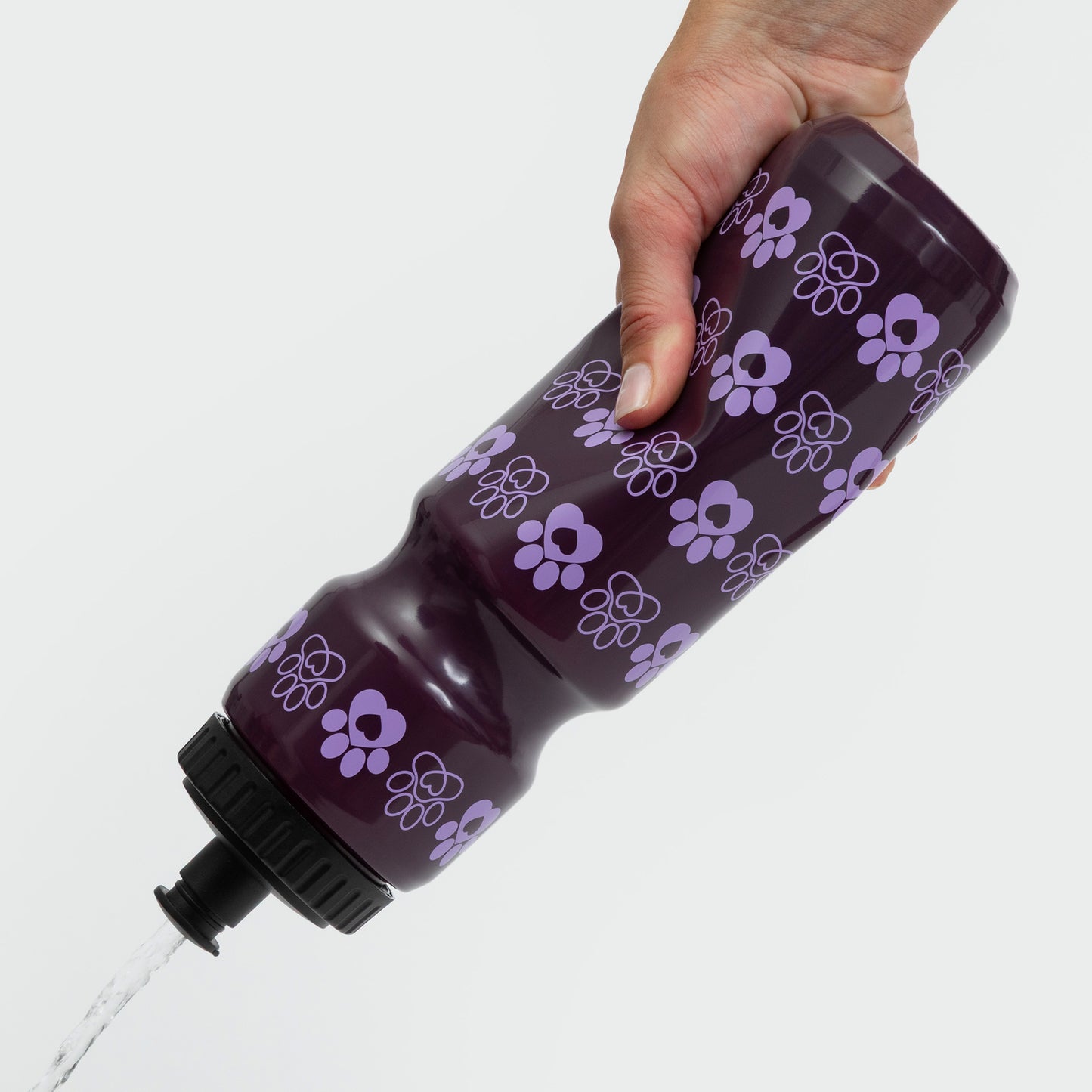 Hand holding a purple water bottle with a floral pattern, water pouring out.