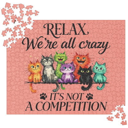 A completed jigsaw puzzle featuring a pink background with the text 'RELAX We're all crazy' and 'IT'S NOT A COMPETITION' in black script. Colorful cartoon cats sit on a branch across the center, and a few loose puzzle pieces are scattered around the corners.