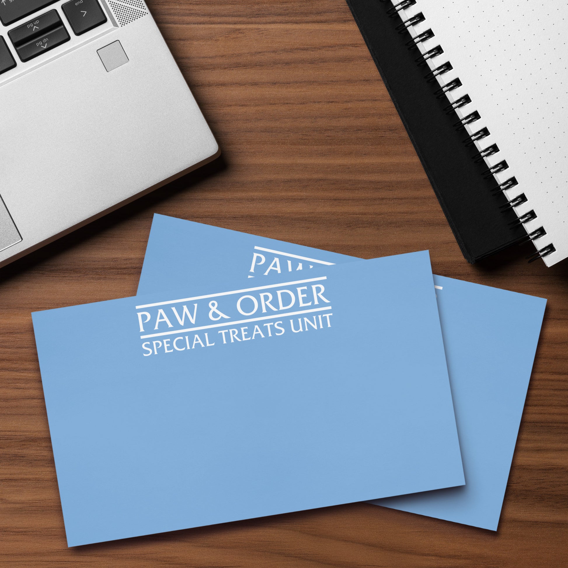 Two sticky note pads with 'Paw & Order Special Treats Unit' text on a wooden surface with a laptop and notebook.