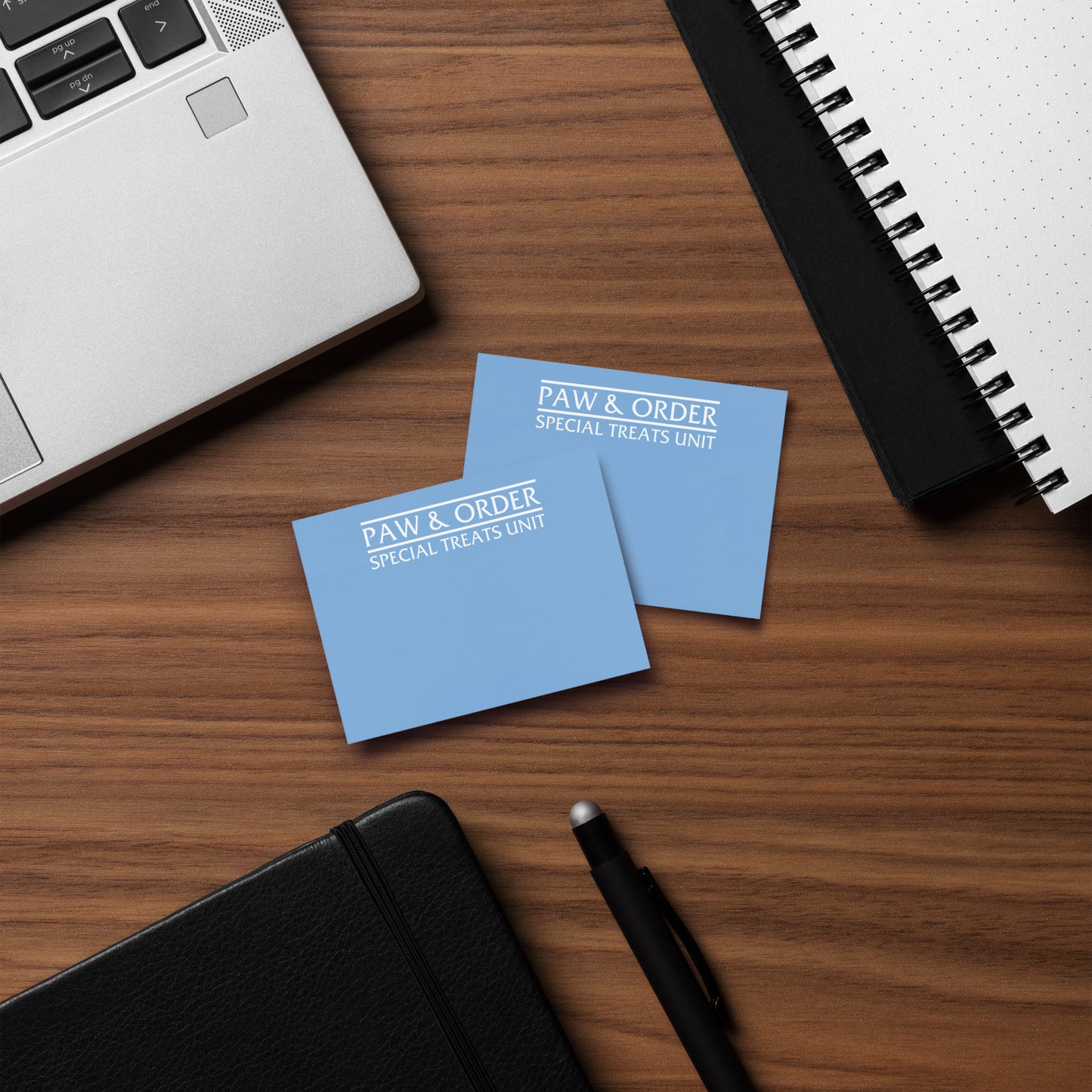 Two blue note pads with 'PAW & ORDER' on a wooden desk with a laptop and notebook.
