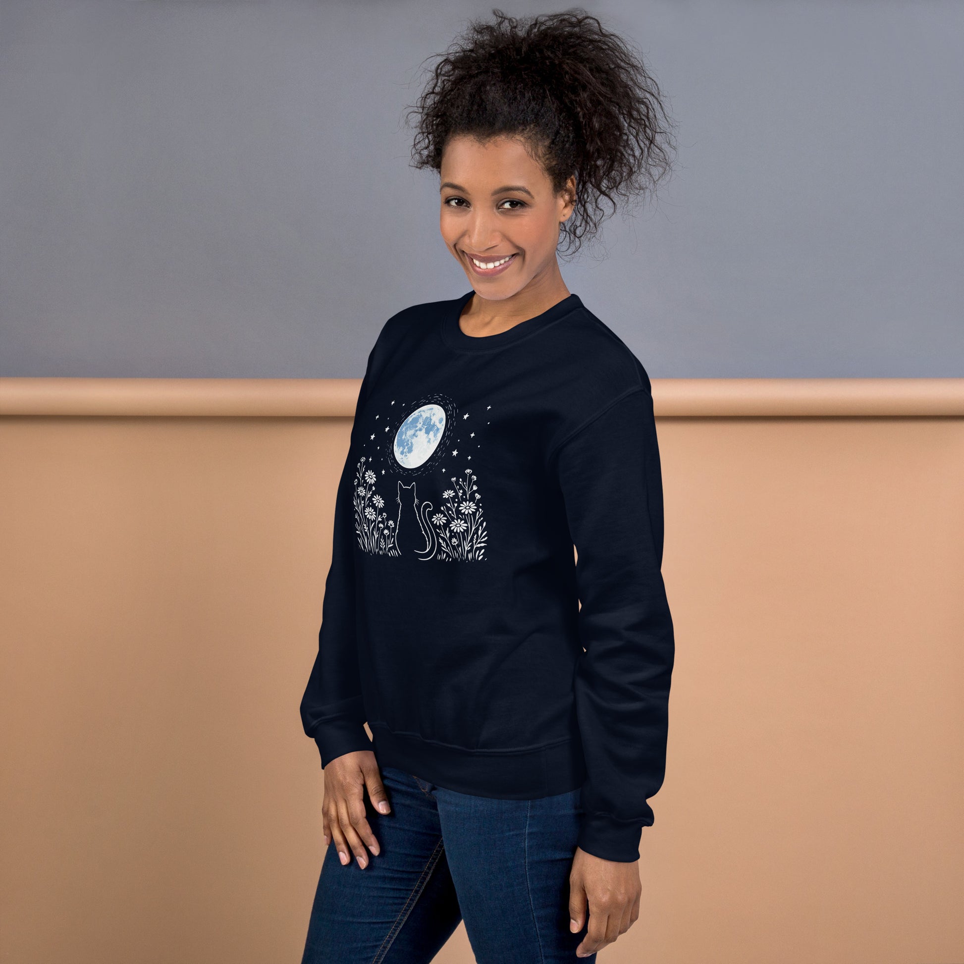 Woman wearing a black sweatshirt with a white cat and moon graphic design on a neutral background