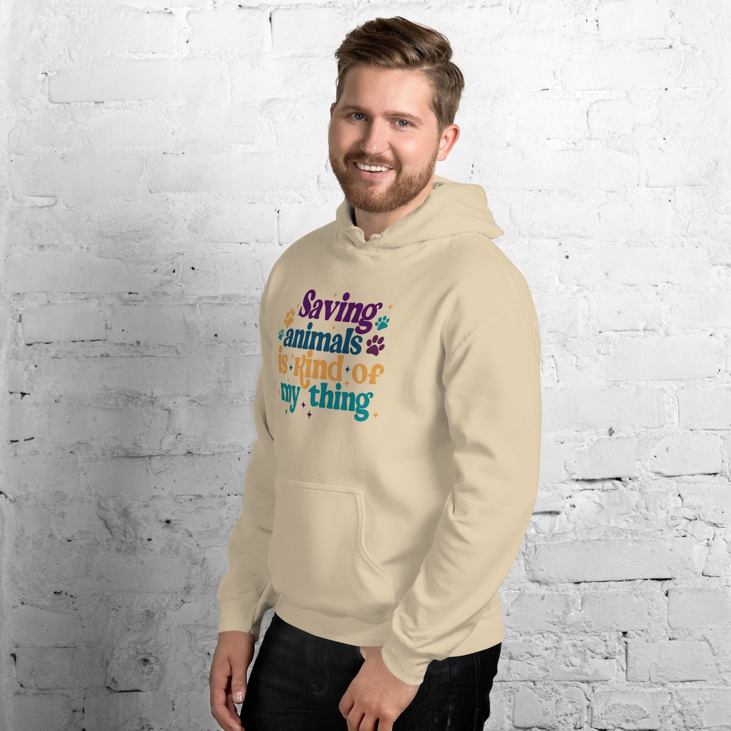 Man wearing a tan Hooded Sweatshirt that reads Saving Animals is kind of my Thing with several paw print and sparkle images in a purple, yellow and blue font.