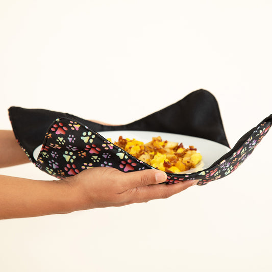 Hands holding a plate resting on a paw printed plate cozy, against a white background.